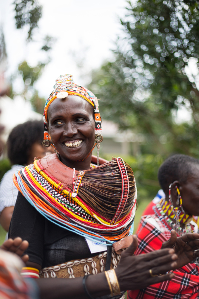 an Indigenous woman dressed in traditional clothing in Kenya smiles in a group of peers