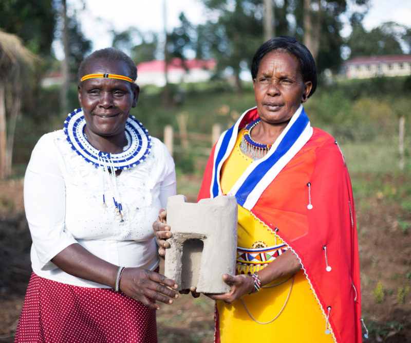 two Indigenous Kenyan women hold a sustainable cooking stove