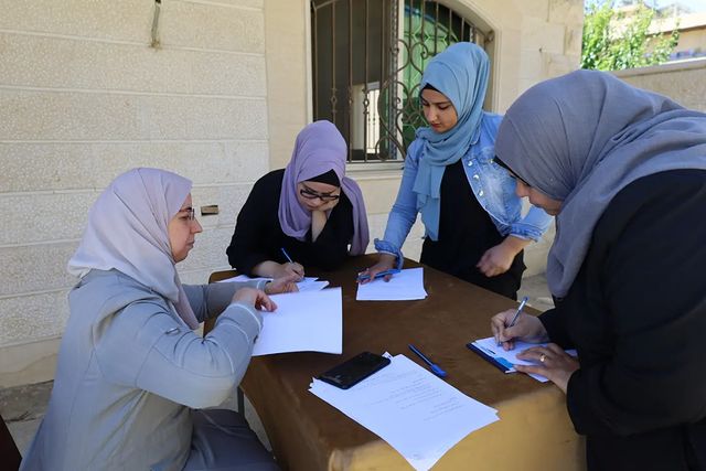 a group of four hijabi women sit around working and writing
