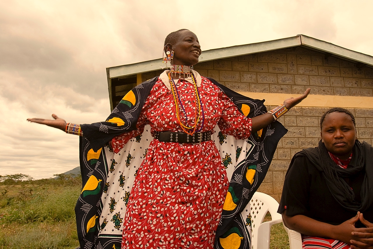 a Maasai woman stands with her arms outstretch at a MADRE training in Kenya