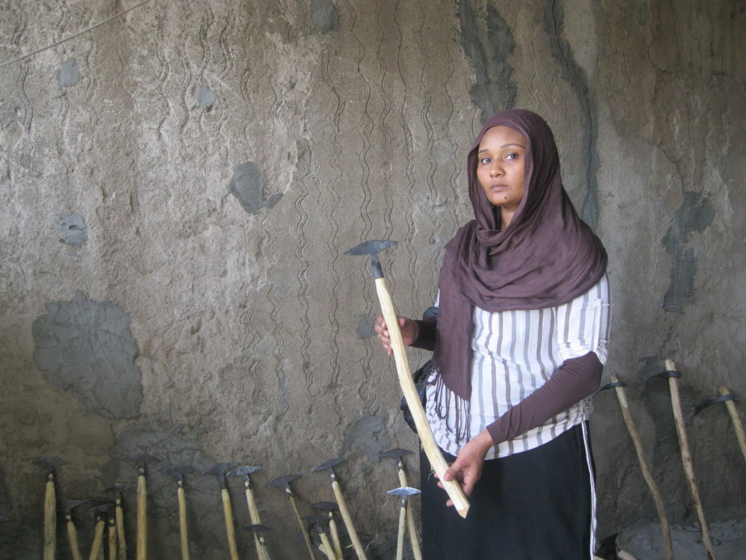 Sudanese woman stands displaying farming tool