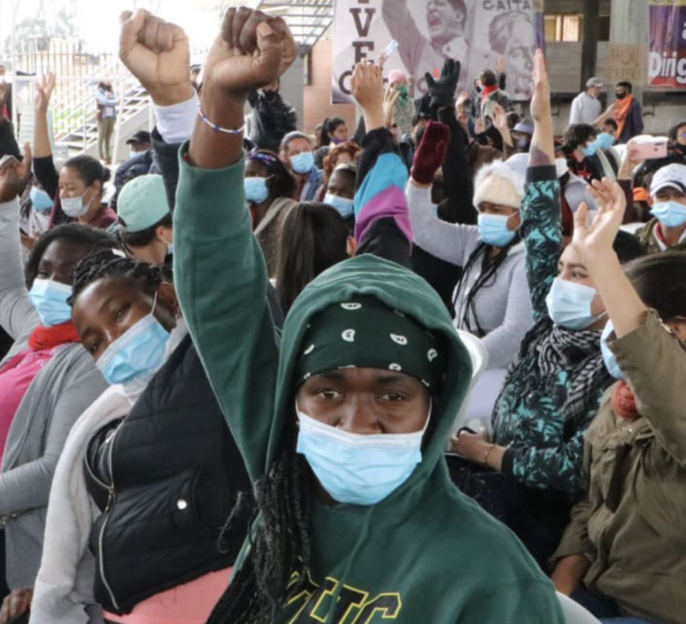 a group of Afro-Colombian women sit with their fits in the air at a protest