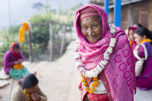 an elderly woman in Nepal dressed in pick stares at camera