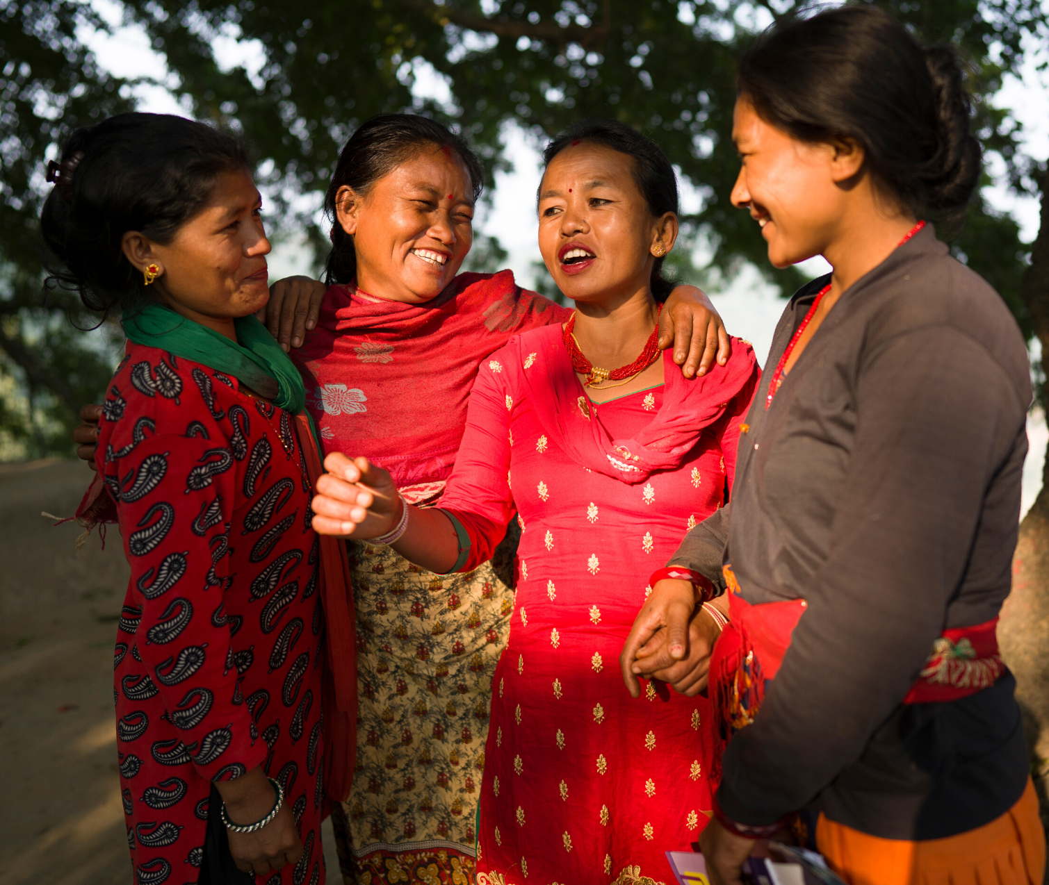 a group of four Nepalese woman hold each other while smiling and chatting