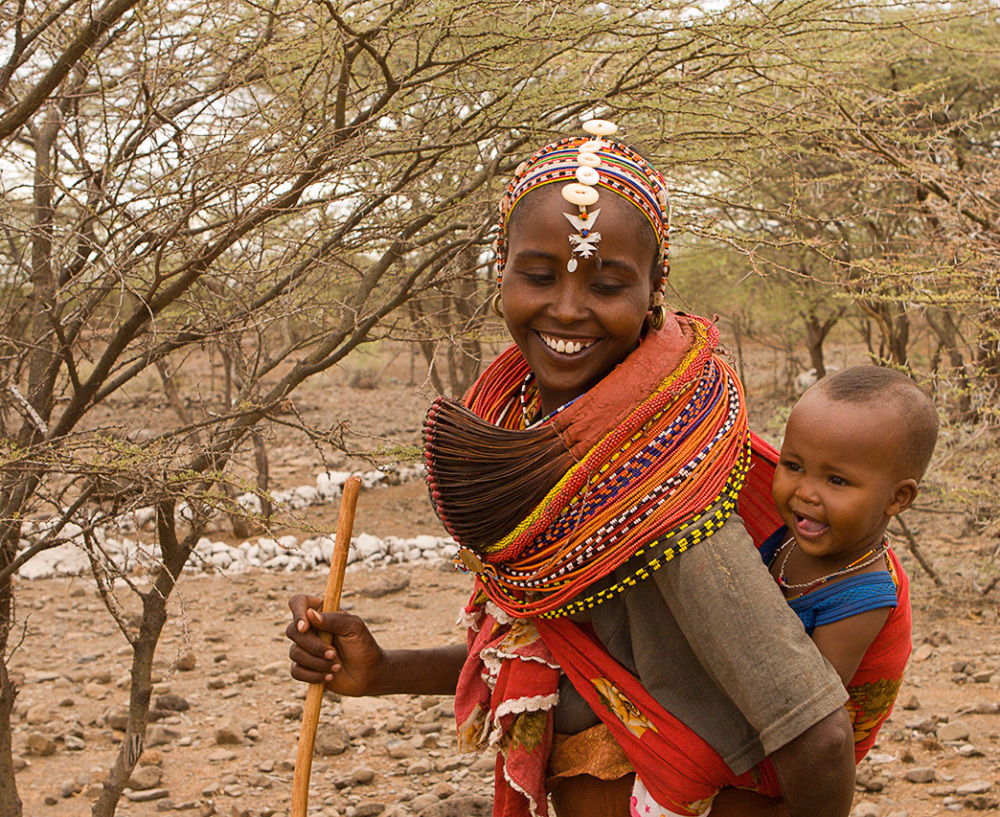 a Indigenous Kenyan woman walks with her infant on her back