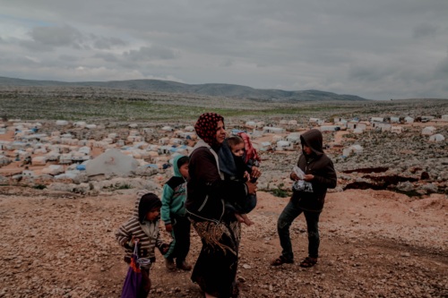 a Syrian mother walks with her four children a top a hill overlooking a refugee camp