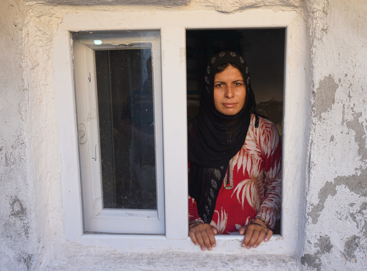 a Syrian woman refugee stand in a window frame looking out