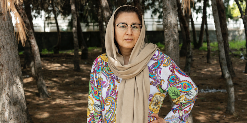 Portrait of Najiba, a woman with dark hair, wearing glasses, a tan headscarf, and floral top.